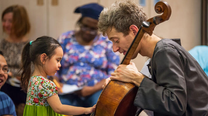 A cellist demonstrates his instrument to a small, excited child