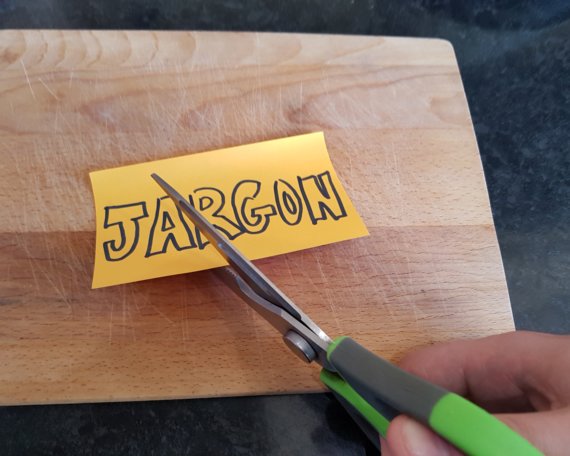 Scissors cut through a post-it with the word 'Jargon' written on it