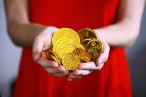 A woman in a red dress holds a handful of large gold coins
