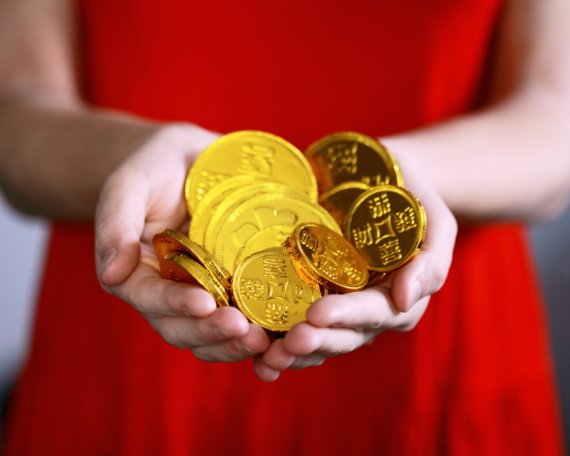 A woman in a red dress holds a handful of large gold coins